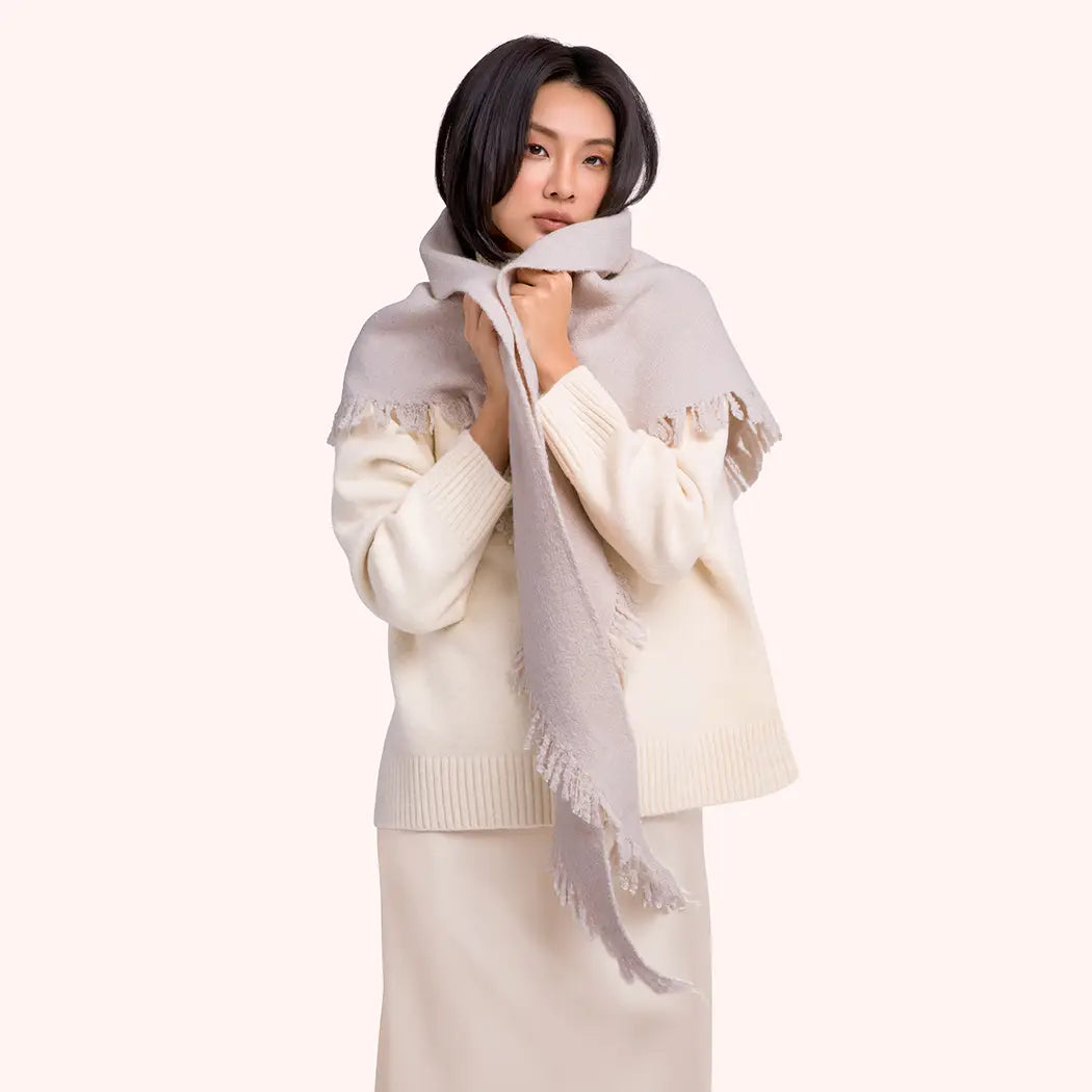 Woman wearing a light-colored scarf and sweater on a white background