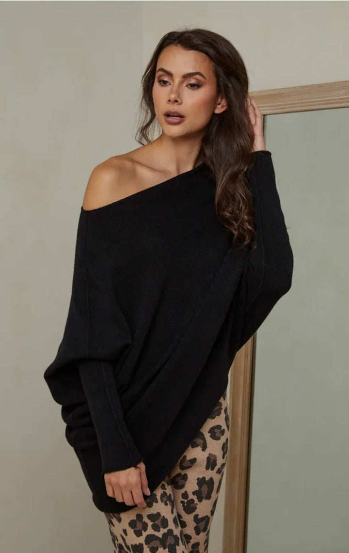 Woman wearing a black off-shoulder sweater and leopard print pants against a plain background