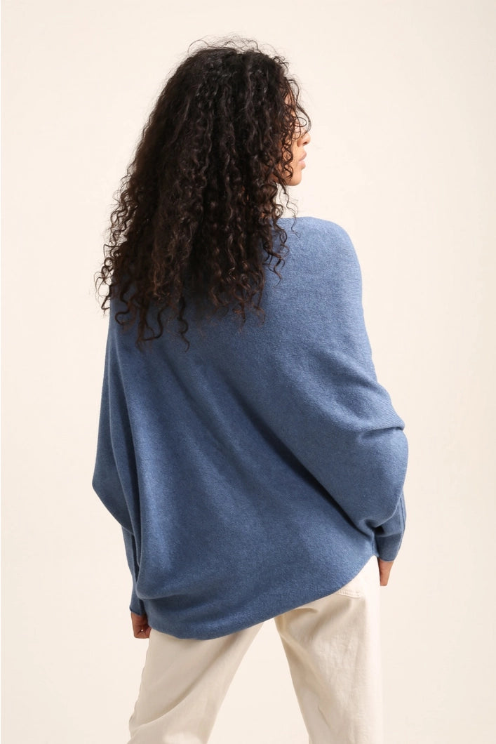 Person wearing a blue sweater and white pants against a beige background