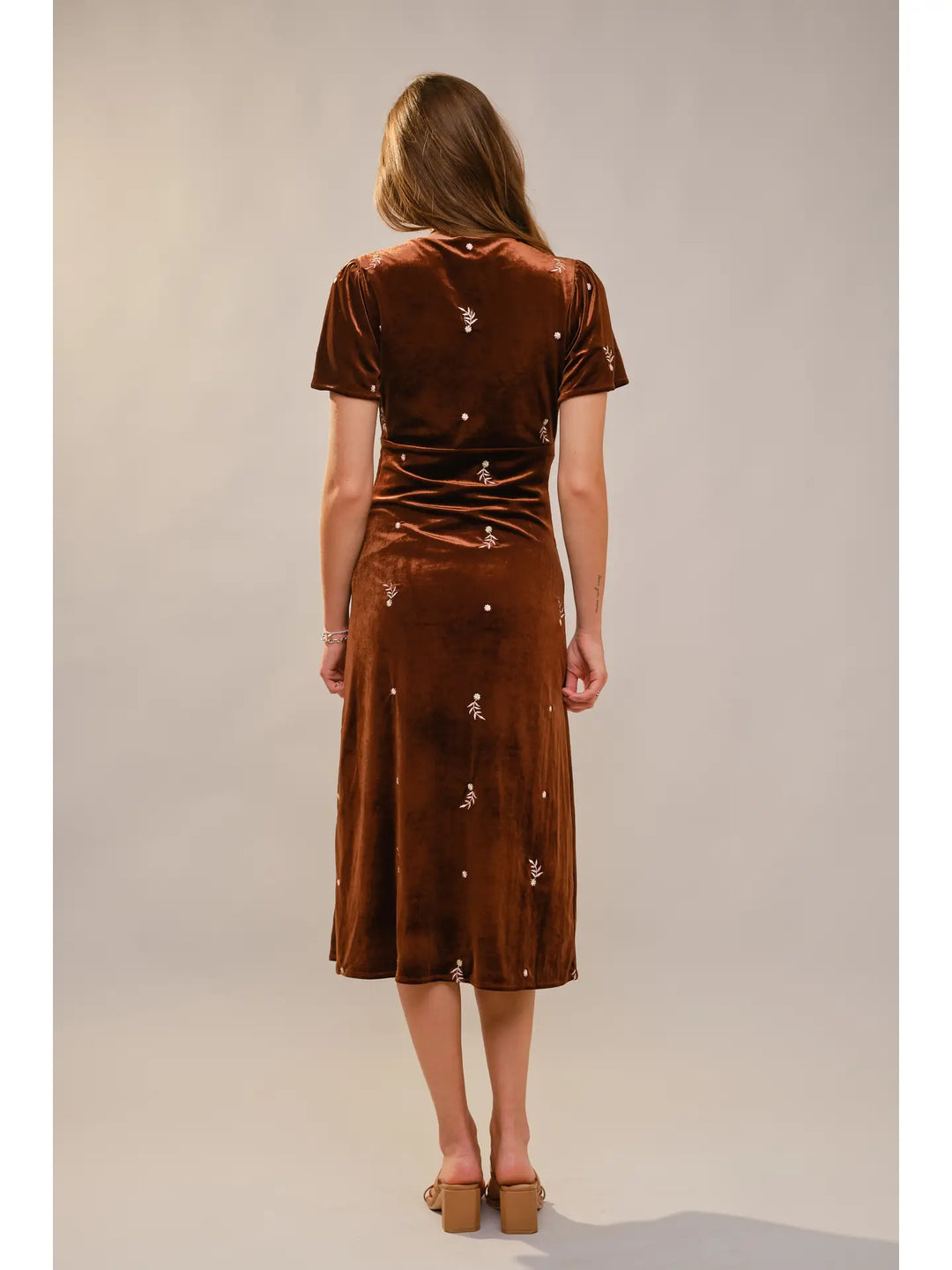 Woman wearing a brown velvet dress with decorative elements on a plain background