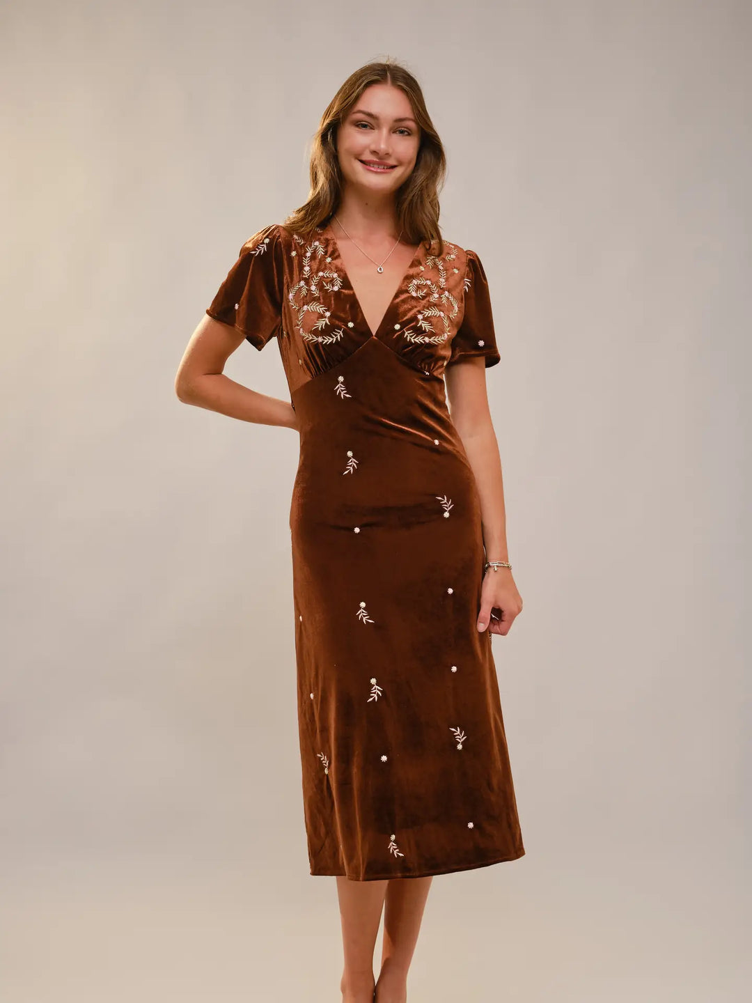 Woman wearing a brown velvet dress with floral embellishments on a plain background
