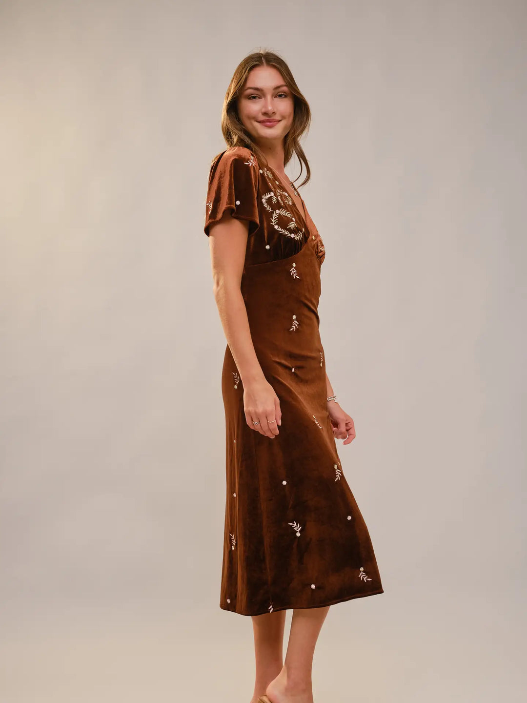 Woman wearing a brown dress with floral embellishments on a plain background