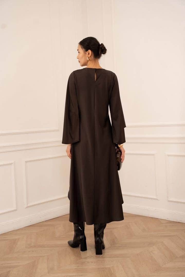 Woman wearing a brown dress standing in a room with white paneled walls and wooden flooring.