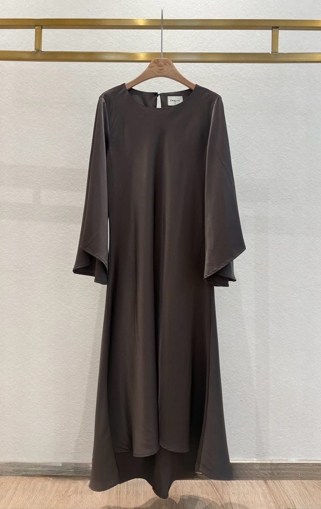 Brown dress hanging on a wooden hanger against a light gray wall.