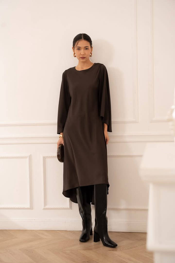 Woman wearing a brown dress and black boots against a white paneled wall.