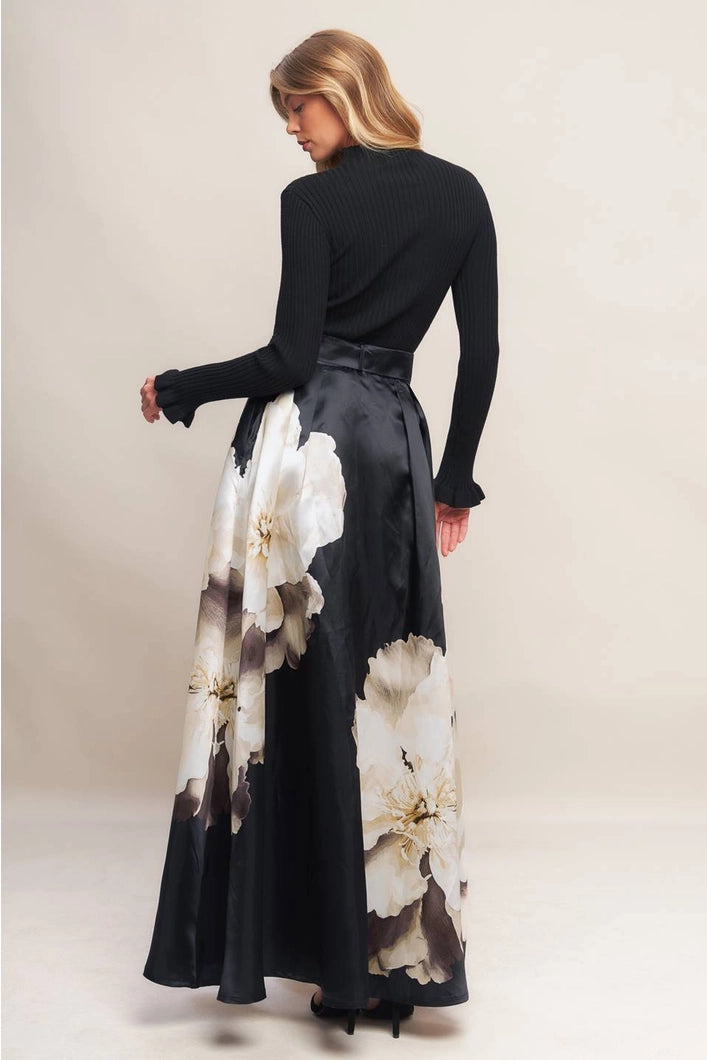 Woman wearing a black top and floral skirt against a plain background
