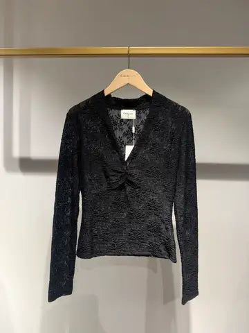 A black textured long-sleeve top with a twisted front detail, hanging on a wooden hanger against a light gray wall.