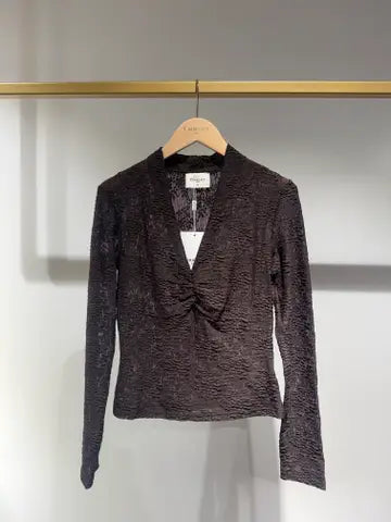 A dark brown textured long-sleeve wrap top with a V-neck and front twist detail, hanging on a wooden hanger branded 'L'AMOUR' against a light gray wall.