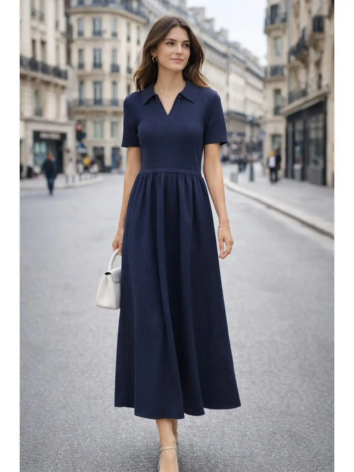 A woman wearing a navy blue midi dress with short sleeves, a V-neckline, and a gathered waist, walking down a city street.