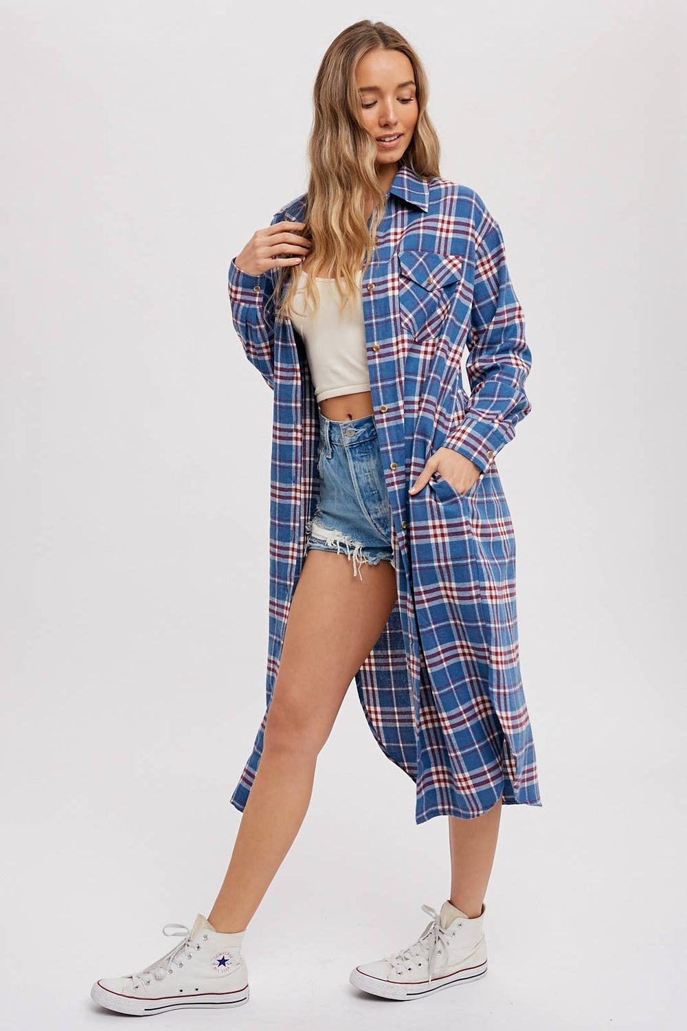 Woman wearing a blue plaid shirt over a white top and denim shorts on a white background
