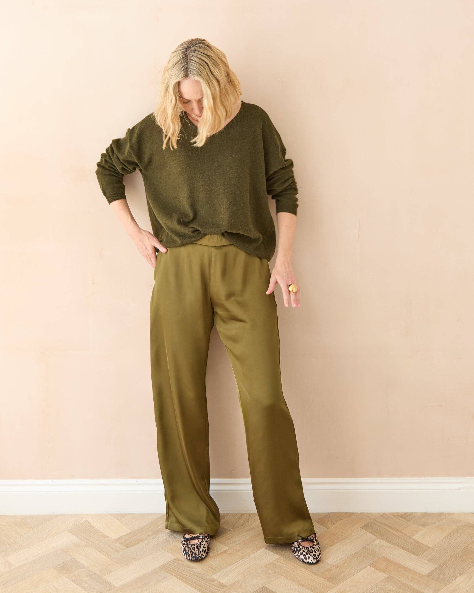 Woman wearing an olive green outfit against a beige wall.