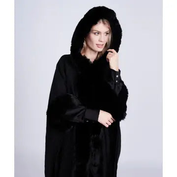A model wearing a black hooded coat with a plush faux-fur collar and cuffs, photographed against a light gray studio background.