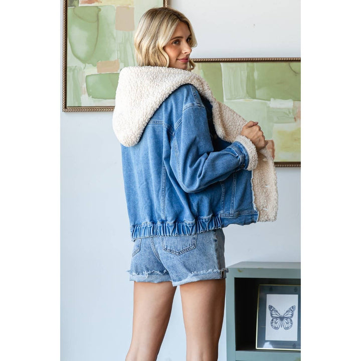 Woman wearing a denim jacket with a white fur hood in a room with abstract art on the wall.