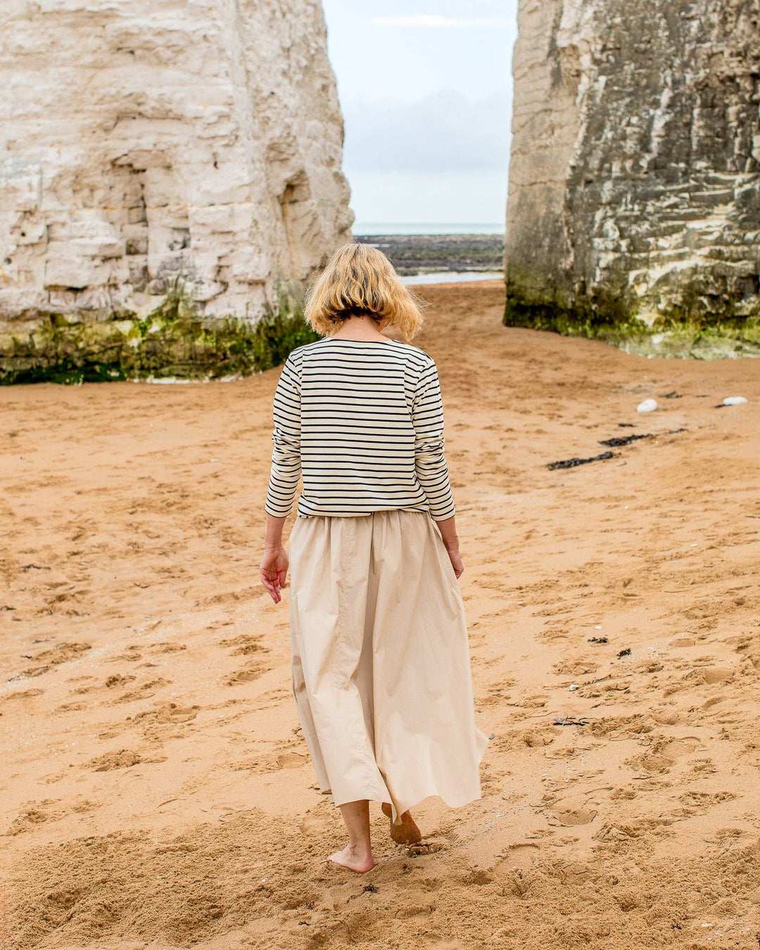 Woman walking on a beach with large rock formations in the background