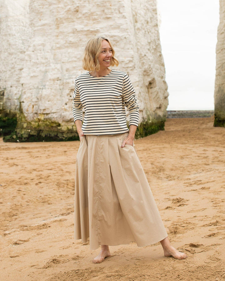 Woman standing on a sandy beach wearing a striped shirt and beige pants.