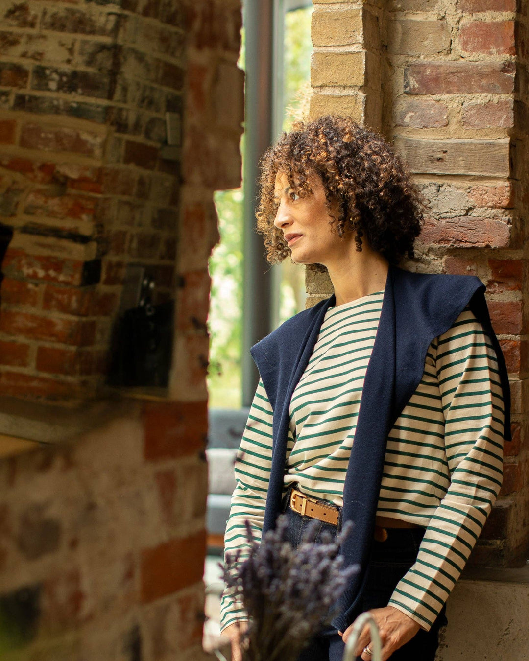 Woman in a striped shirt and navy cardigan standing against a brick wall.
