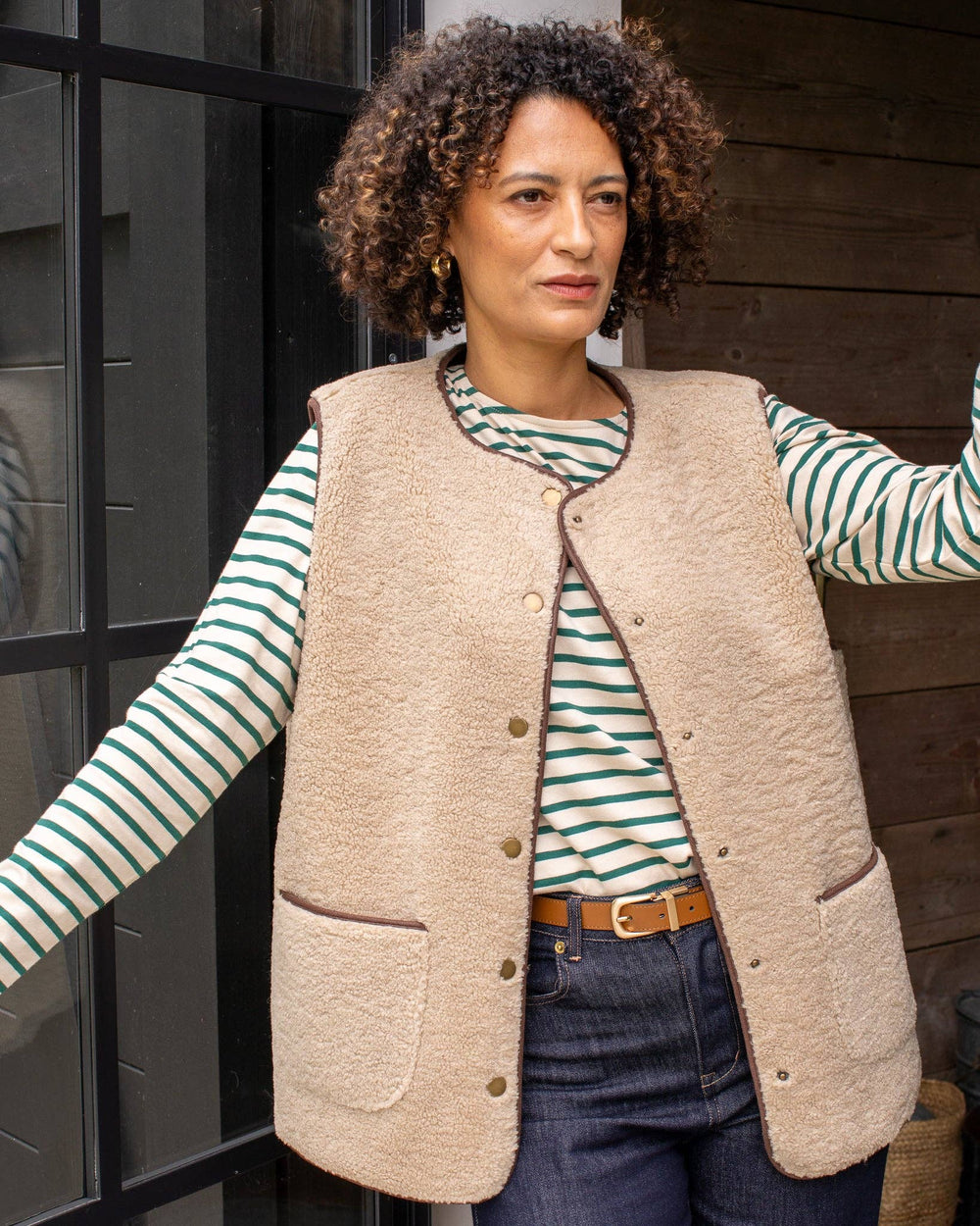 Woman wearing a beige vest over a striped shirt with a wooden background