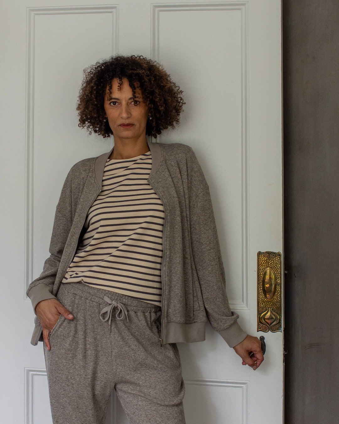 Woman wearing a striped shirt and gray cardigan standing in front of a white door.