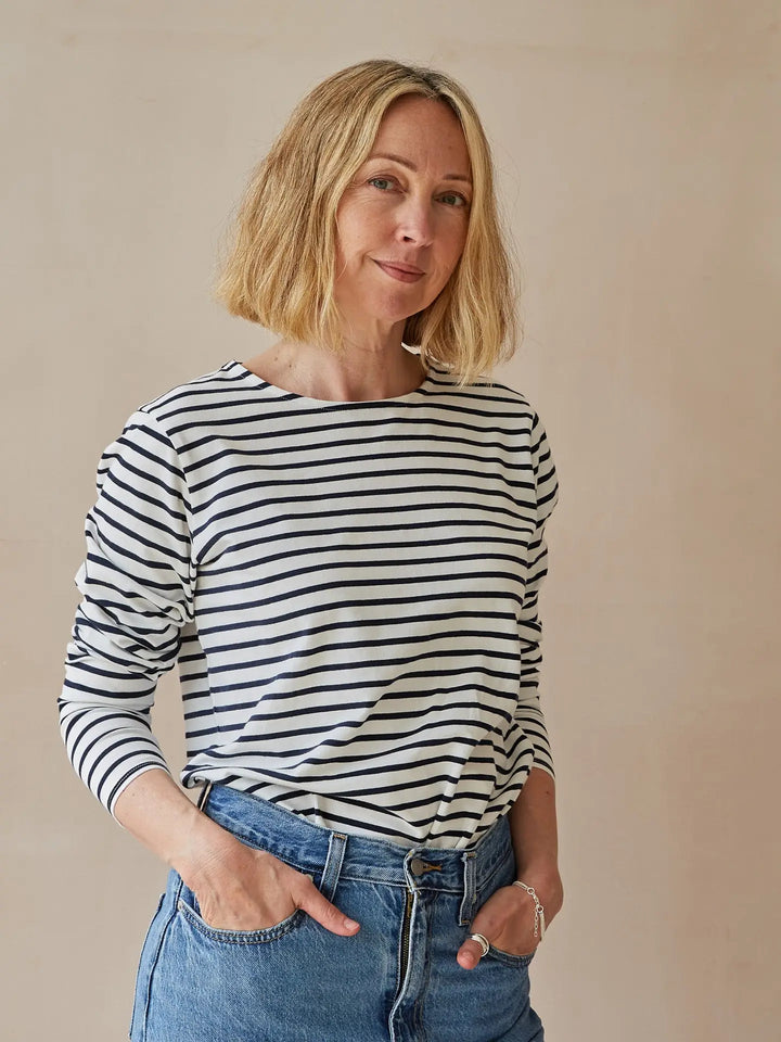 Woman wearing a black and white striped shirt and blue jeans against a beige background