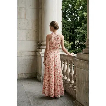 Woman in a floral dress standing on a stone balcony with columns and greenery.