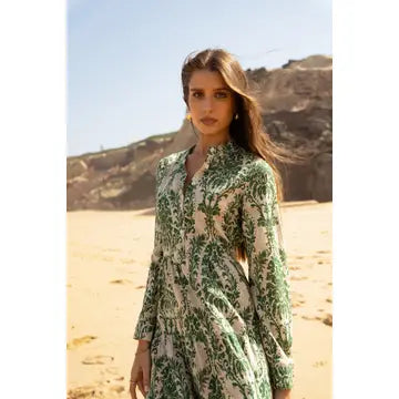 A woman stands in a sandy desert landscape wearing a long-sleeve collared dress with a green and cream botanical pattern.