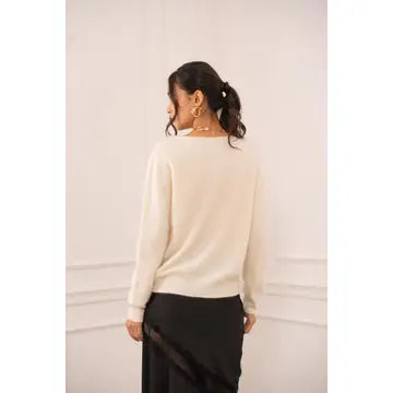 A woman shown from the back wearing a cream-colored knit sweater and a black skirt, standing against a light-colored wall with decorative molding.