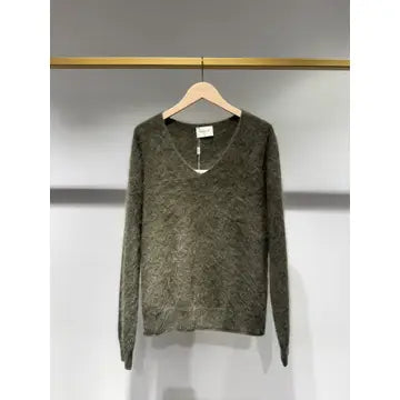A fuzzy, textured knit sweater in a muted olive-brown color, hanging on a wooden hanger against a gray wall.