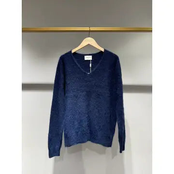 A dark blue long-sleeve knit sweater with a V-neckline, hanging on a wooden hanger from a gold clothing rack against a light gray wall.