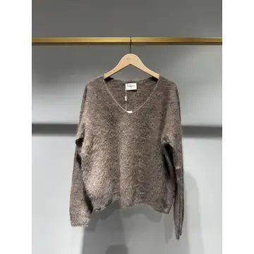 A fuzzy, textured knit sweater in a taupe-brown color, hanging on a wooden hanger against a gray wall.