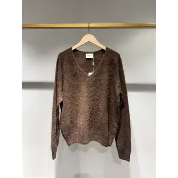 A brown fuzzy knit sweater with a V-neck and long sleeves, hanging on a wooden hanger against a light gray wall.