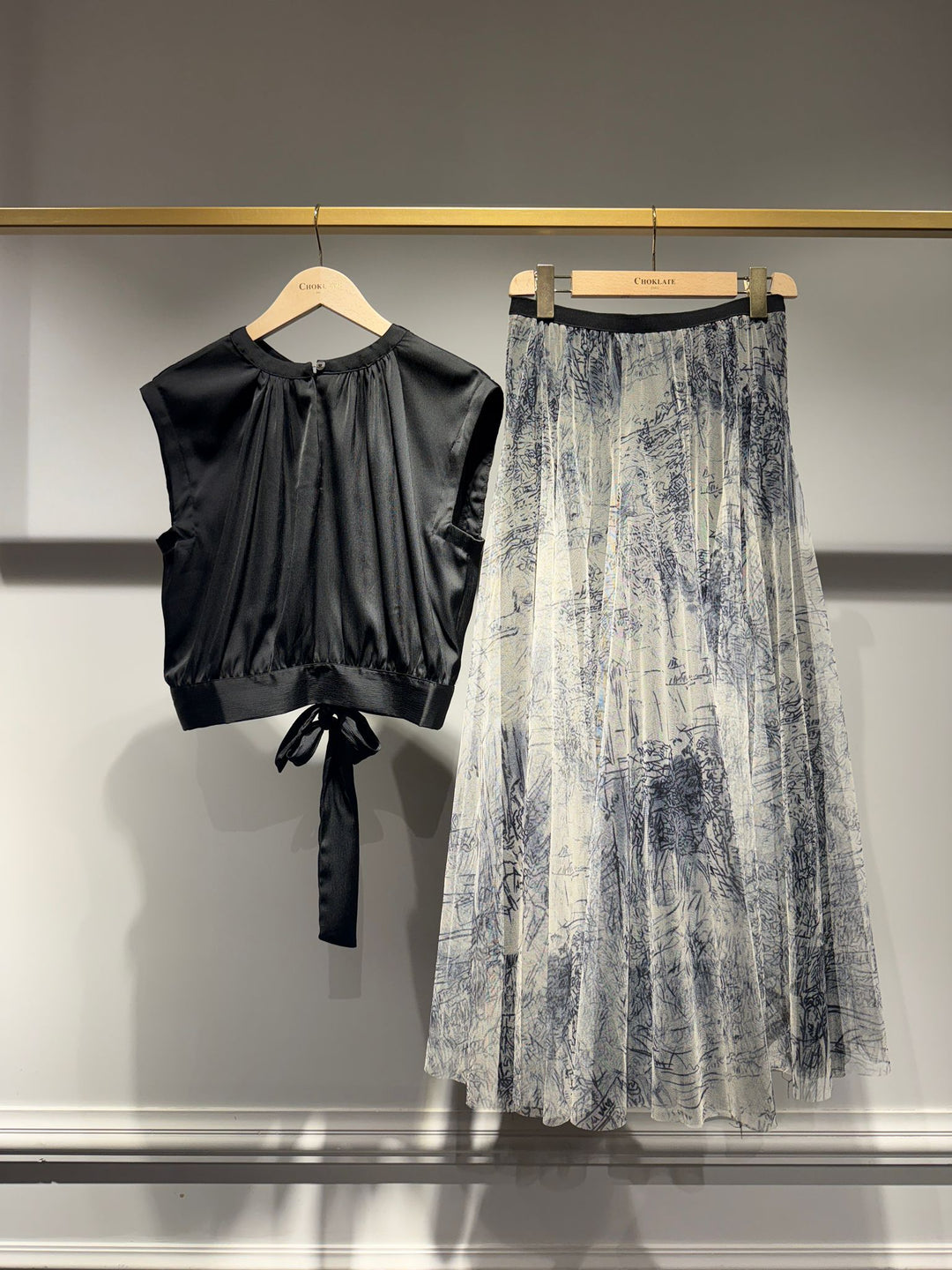 Black top and patterned skirt on hangers against a gray background