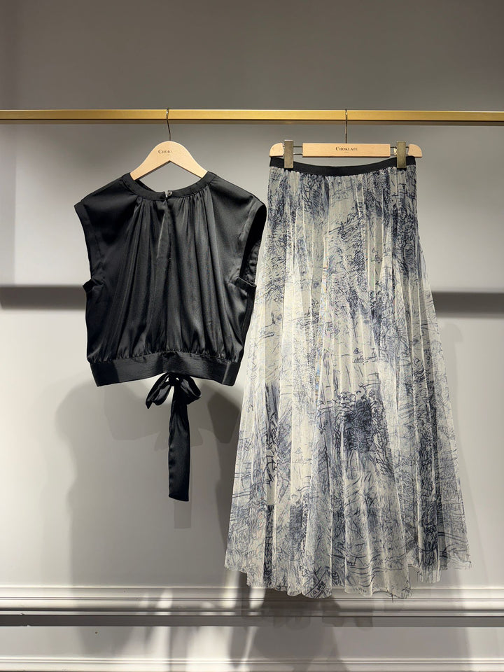 Black top and patterned skirt on hangers against a gray background