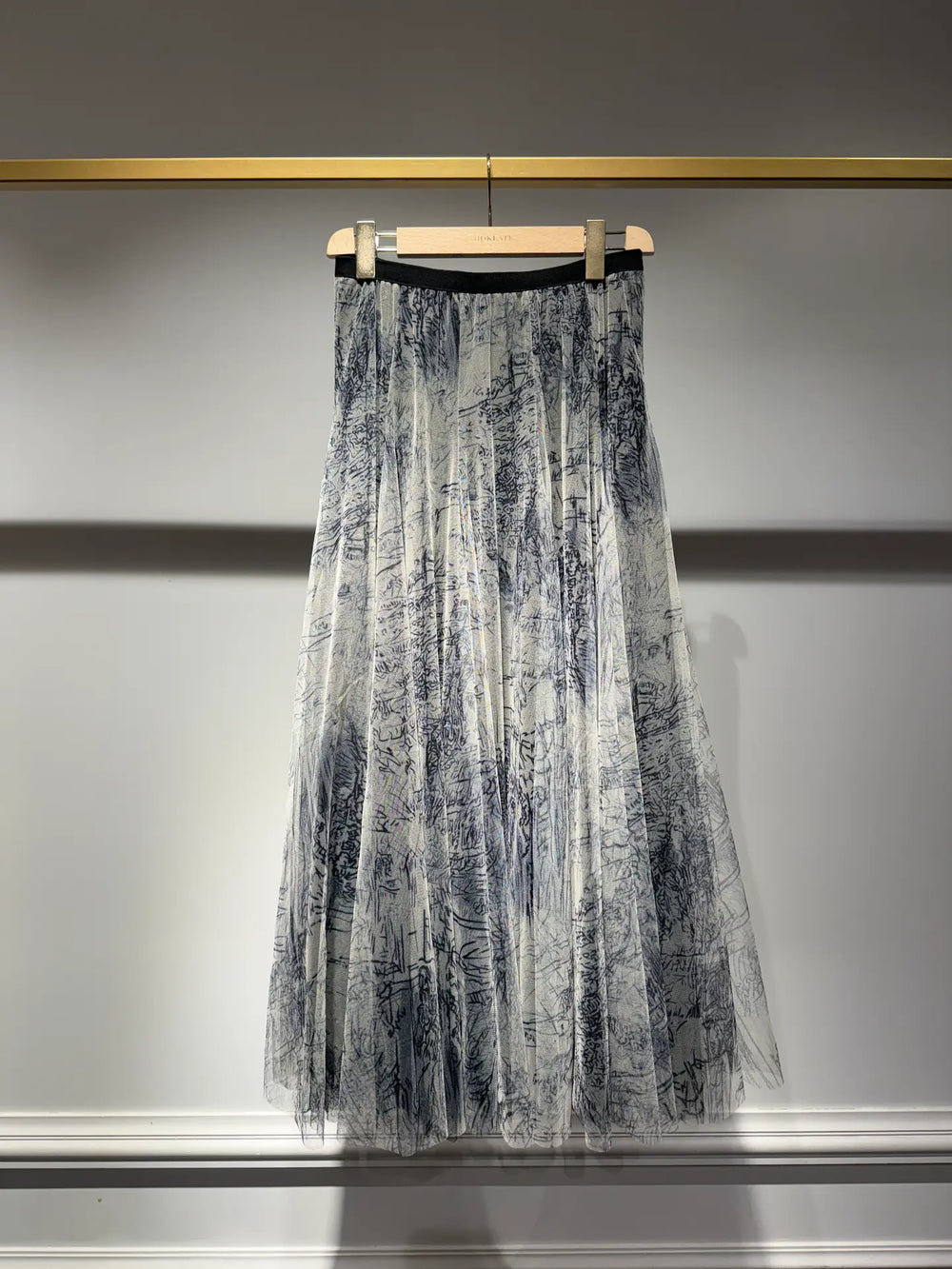 Translucent black and white patterned skirt hanging on a rack against a neutral background