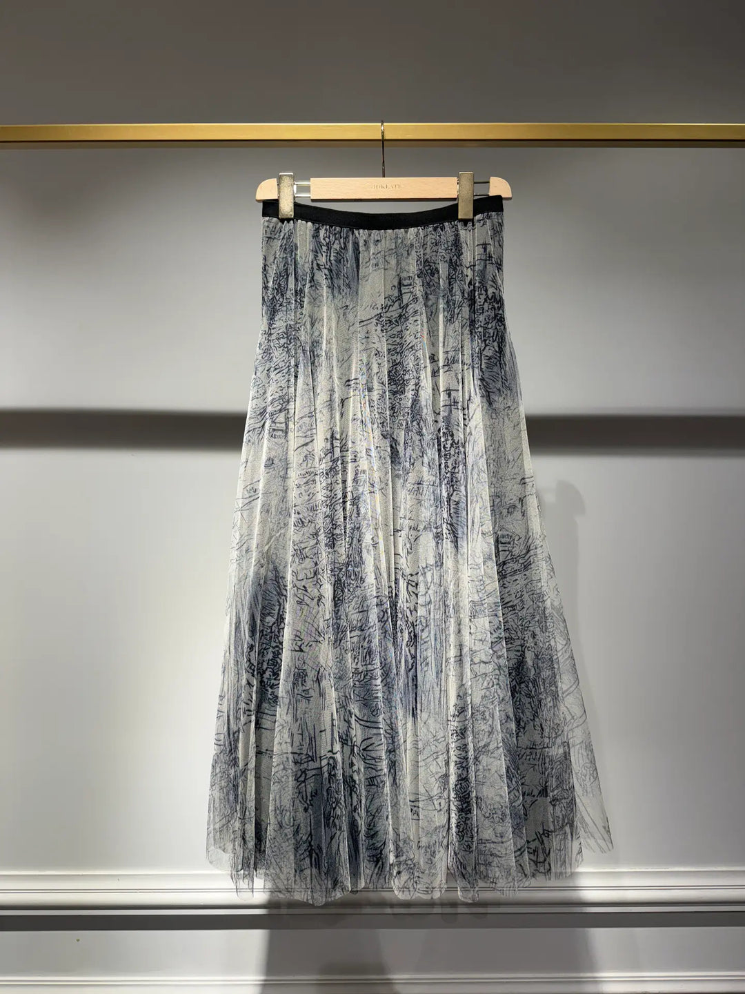 Translucent black and white patterned skirt hanging on a rack against a neutral background