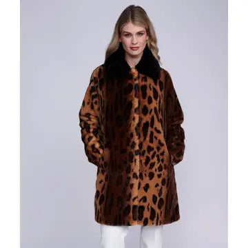 A woman modeling a brown leopard-print faux fur coat with a black collar, paired with white pants, against a light gray studio background.