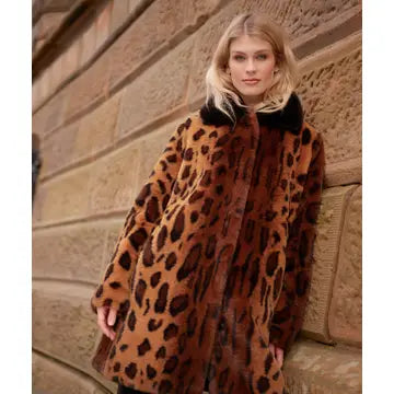 A woman wearing a brown and black leopard-print faux fur coat with a black collar, standing against a stone wall.
