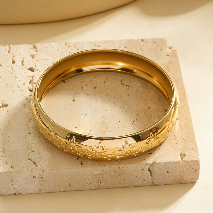 Gold bracelet with embossed design on a beige stone surface