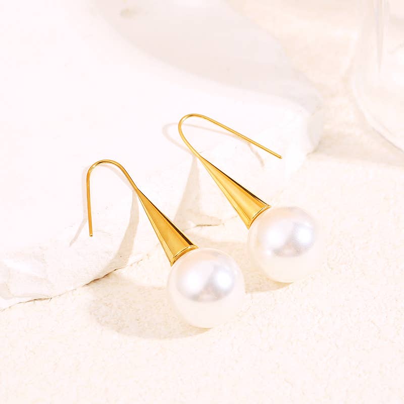 Gold earrings with pearl drops on a soft beige background