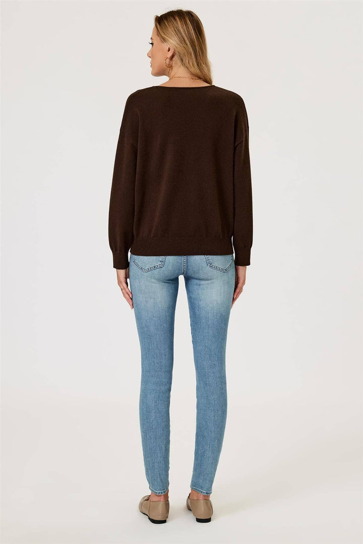 Woman wearing a brown long-sleeve top and light blue jeans on a white background