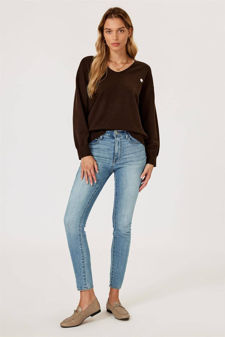 Woman wearing a brown sweater and light blue jeans on a white background