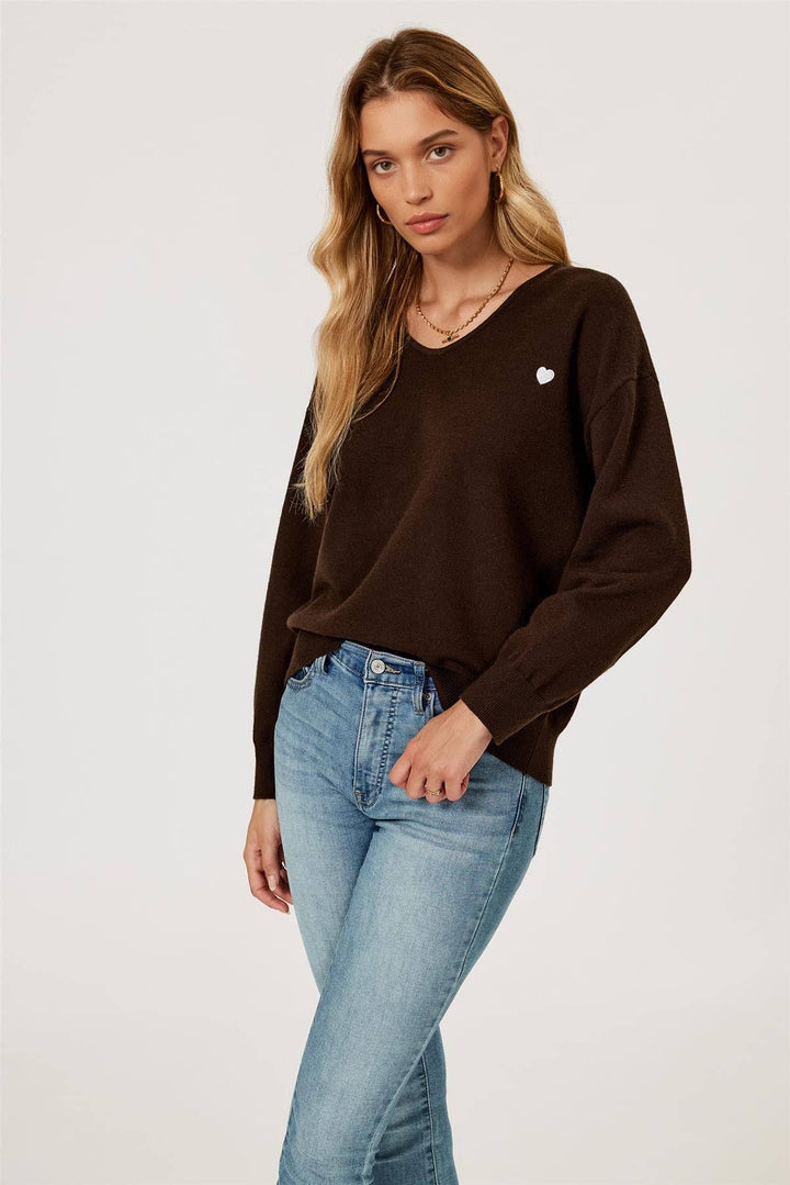 Woman wearing a brown sweater with a heart emblem and light blue jeans on a white background