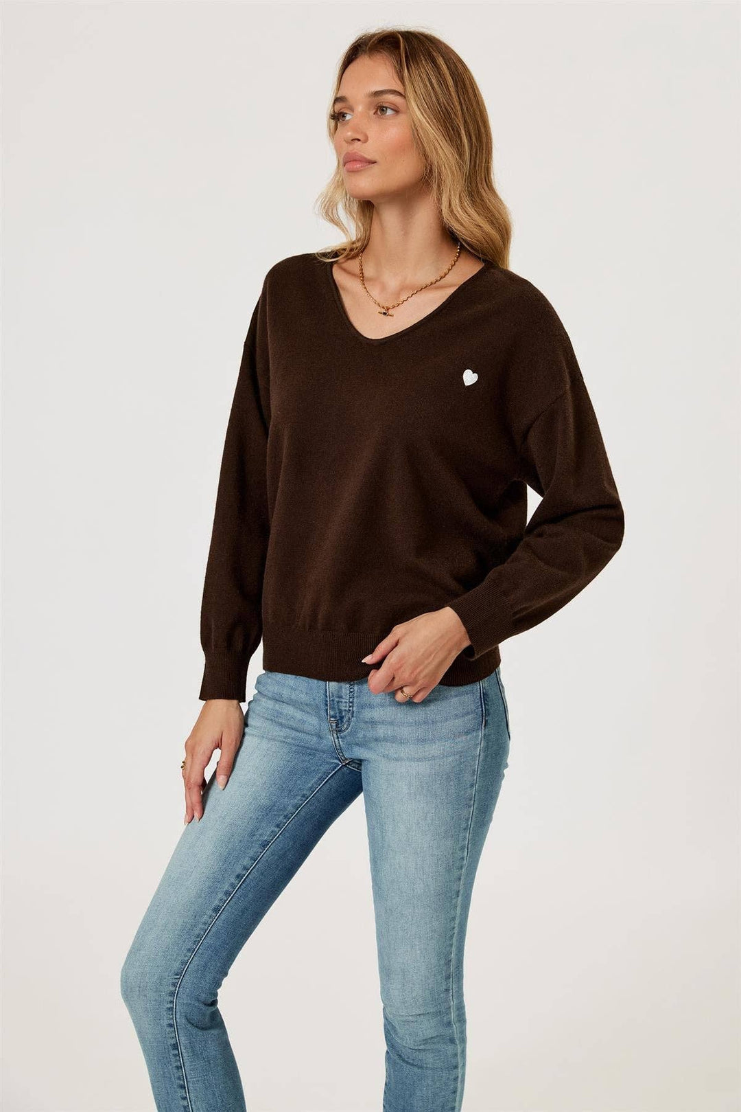 Woman wearing a brown sweater and light blue jeans on a white background