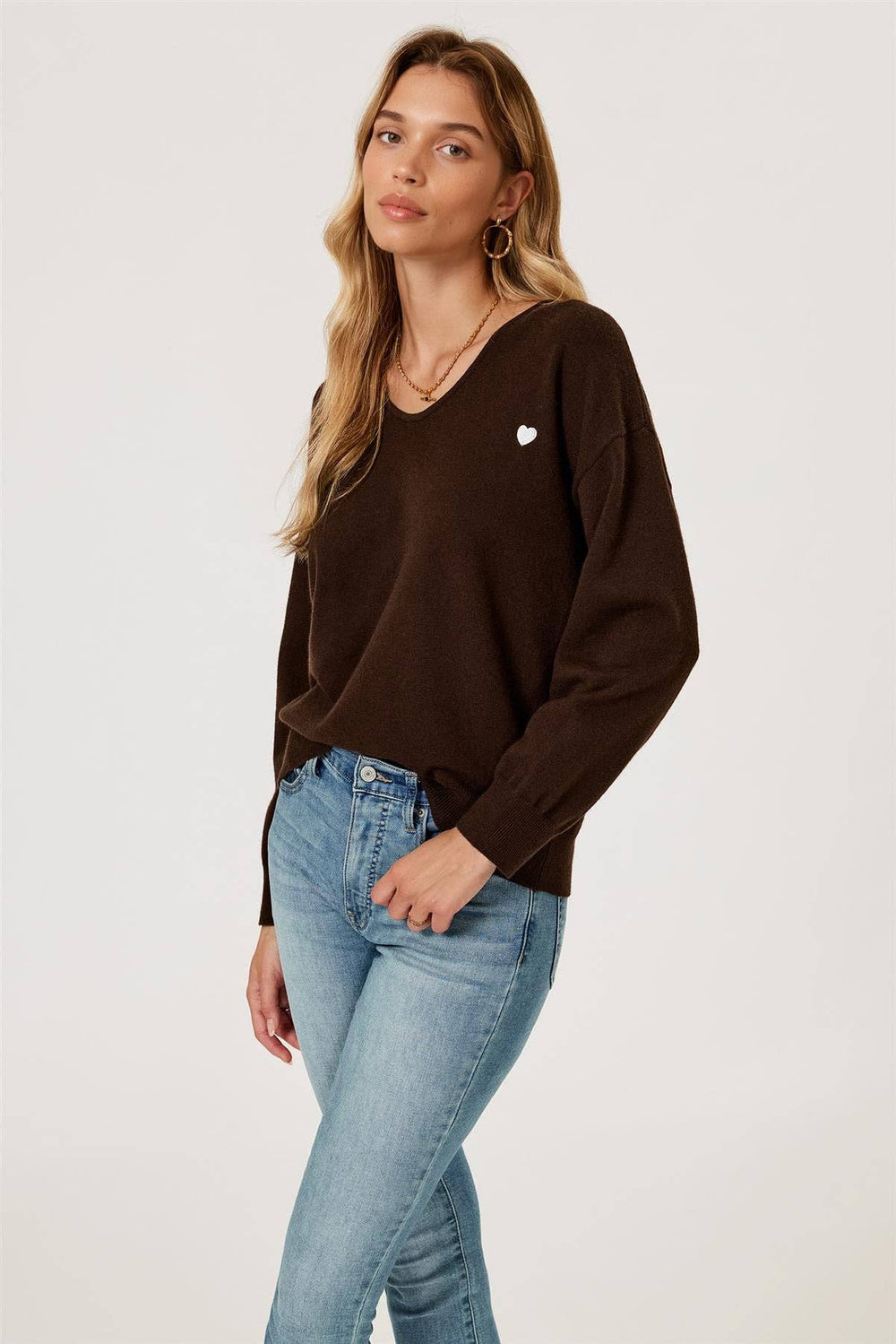 Woman wearing a brown long-sleeve top and light blue jeans on a white background