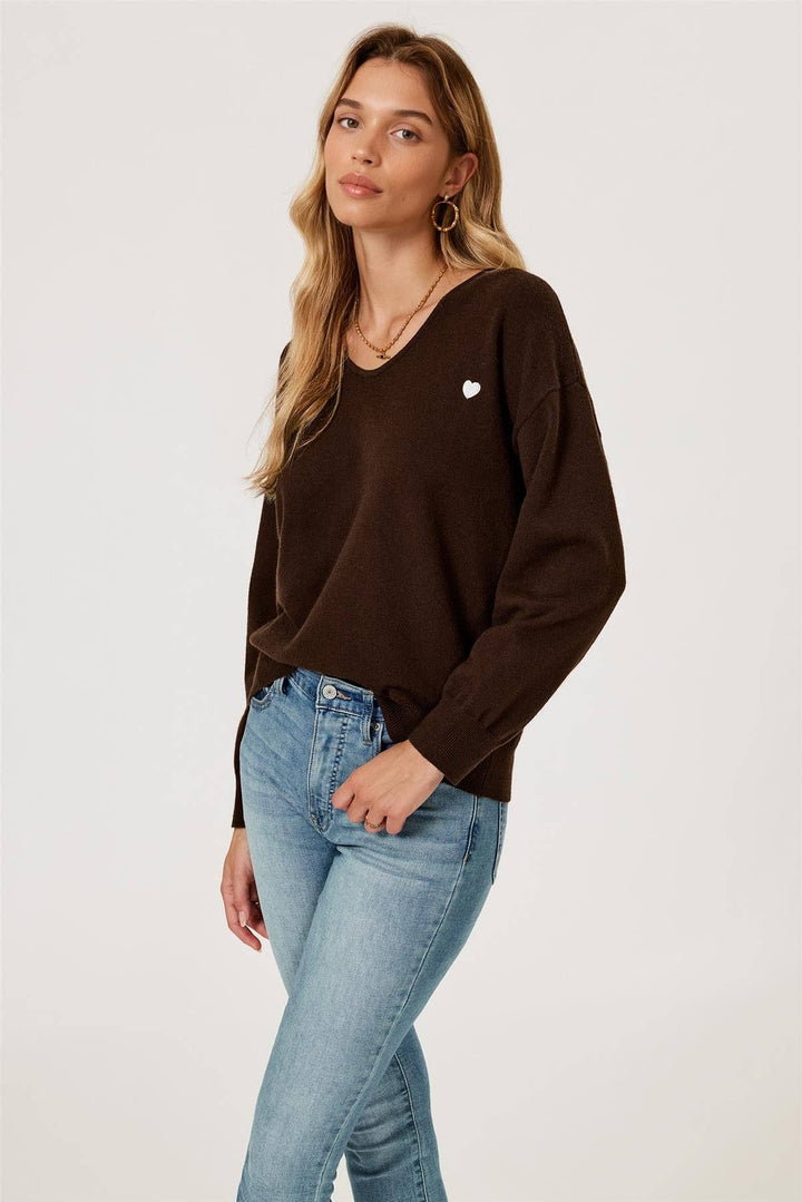 Woman wearing a brown long-sleeve top and light blue jeans on a white background