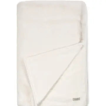 A folded cream-colored plush throw blanket with a small silver-gray brand tag on the bottom right corner, set against a plain white background.