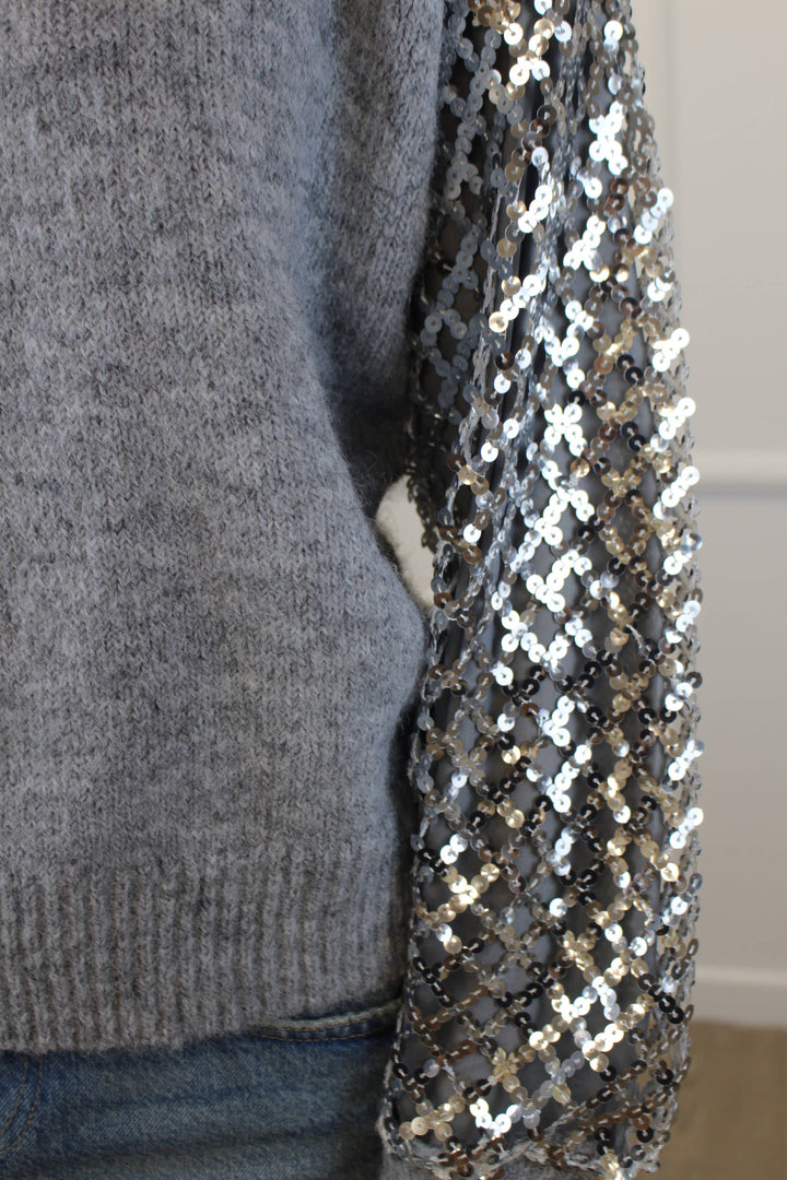 Gray sweater with a sequined sleeve against a neutral background