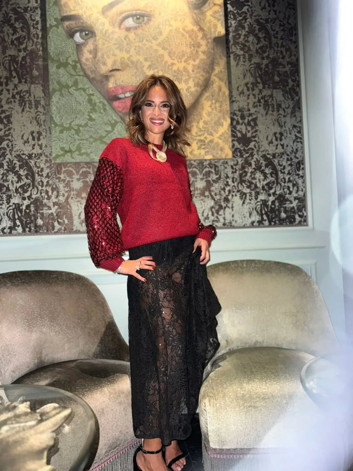 Woman in a red sweater and black lace skirt standing in a room with a textured wall and sofa.
