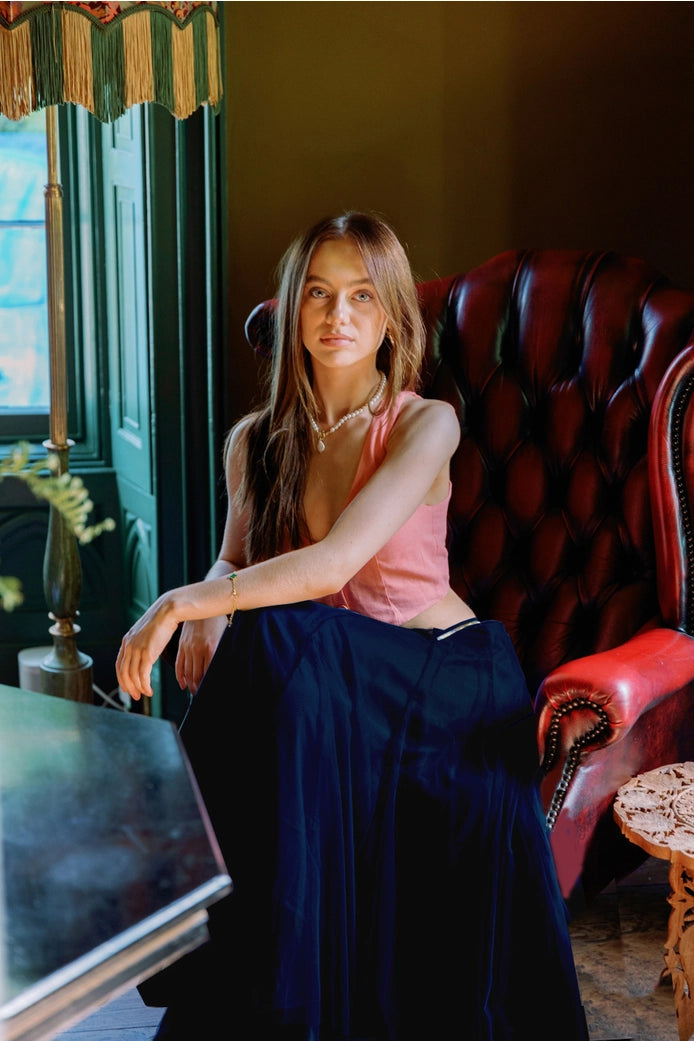 Woman sitting on a red leather chair in an elegant room with a window and decorative elements.