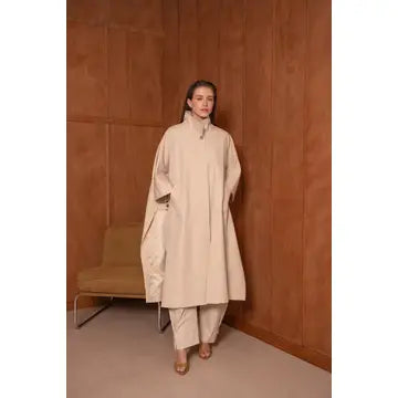 Woman wearing a beige outfit against a brown wall.