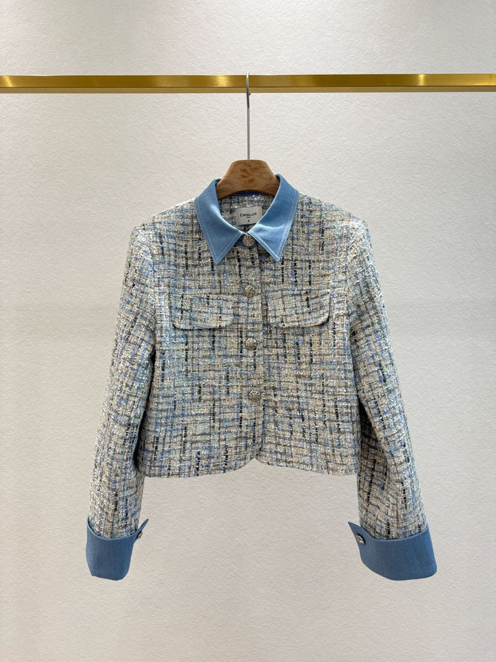 Tweed jacket with blue collar and cuffs on a hanger against a light gray background